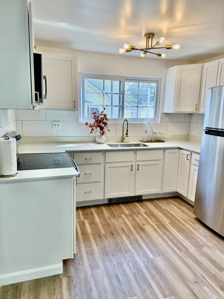 Renovated kitchen with white cabinets, sink beneath the window, and stainless steel refrigerator