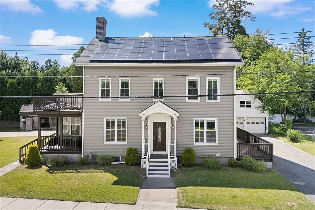 Front view of a gray two-story house with white trim, porches, and solar panels